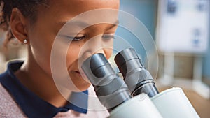 Portrait of Smart Little Schoolgirl Looking Under the Microscope. In Elementary School