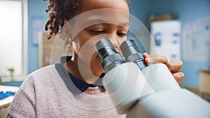 Portrait of Smart Little Schoolgirl Looking Under the Microscope. In Elementary School