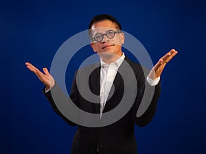 Portrait of smart middle-aged asian confident successful businessman wearing suit with welcoming gesture on blue background