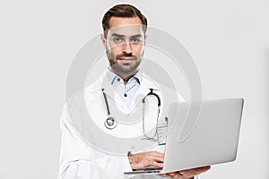 Portrait of smart young medical doctor with stethoscope working in clinic and holding laptop