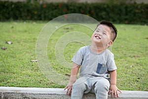 Portrait of smile asian baby boy sitting on the edge of the footpath in park.