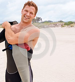 Portrait, smile and man in wetsuit at beach for sports surfing, fitness or exercise on summer vacation. Travel, health