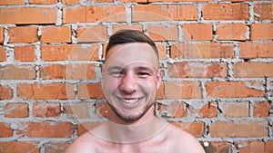 Portrait of smiles young guy with naked torso standing on red brick wall background. Close up of strong bearded man