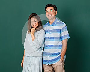 Portrait of a smiley happy loving Asian couple dressed casually standing relaxedly, smiling to a camera for studio shot over green