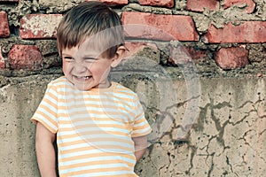 Portrait of a smiling 2 years old boy on a brick wall background. A pretty child smiles and looks away.