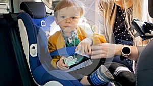 Portrait of smiling 2 years old boy with toy sitting in car safety seat