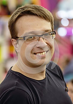 Portrait of a smiling 30-35-year-old man wearing glasses and a T-shirt on a multicolored background.