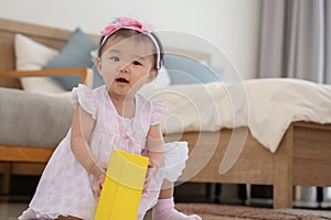 Portrait of smiling adorable Asian baby have fun playing box toys, sitting on floor at bedroom at home. Little toddler girl wear