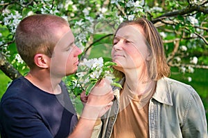 Portrait of a smiling adult woman and a young man walking in a spring apple orchard