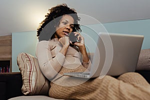 Portrait smiling african american businesswoman using laptop computer and talking with cellphone