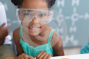 Portrait of smiling african american elementary schoolgirl wearing protective eyewear in laboratory