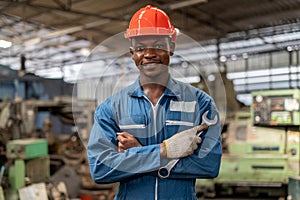 Portrait of smiling African American industrial worker man with helmet crossed arms holding wrench industry factory .happy