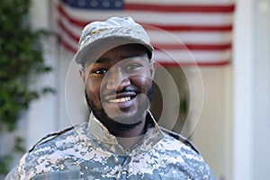 Portrait of smiling african american male soldier standing in front of american flag outside home