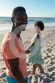 Portrait of smiling african american man holding hand with girlfriend at beach on sunny day