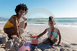 Portrait of smiling african american mother and daughter making sandcastles at beach