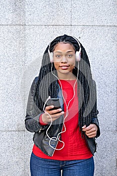 Portrait of a smiling African-American woman with a cell phone is chatting or listening to music on the streets of the city. The