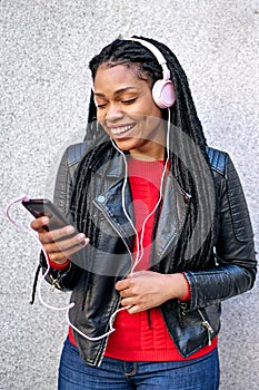 Portrait of a smiling African-American woman with a cell phone is chatting or listening to music on the streets of the city. The