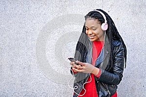 Portrait of a smiling African-American woman with a cell phone is chatting or listening to music on the streets of the city. The