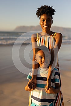 Portrait of smiling african american young woman holding son's hands against sea and clear sky