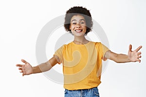 Portrait of smiling african girl reaching hands, inviting you into her embraces, hugging, standing over white background