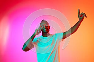 Portrait of smiling african man looking at camera and moves his hands to the side over gradient colorful background in