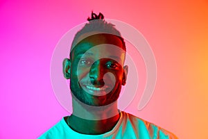 Portrait with smiling african man looking at camera over gradient colorful background in neon.