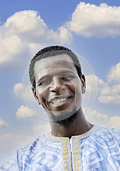 Portrait of a smiling African man wearing a boubou in the street, blue sky, white clouds, photo