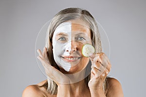 Aged woman with mask on face holding slice of cucumber