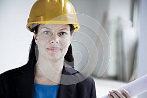 Portrait of smiling architect in a hardhat holding a rolled up blueprint indoors, close-up