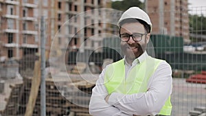 Portrait of smiling architect man standing on the construction site with crossed hands looking at the camera. Outside