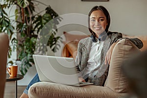 Portrait of smiling asian business woman working laptop sitting in cozy office