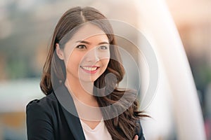 Portrait of a smiling asian businesswoman standing with arms folded on blurred city background. Business concept