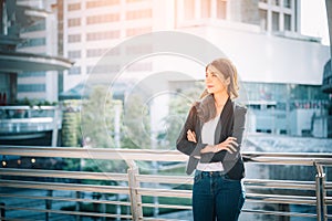 Portrait of a smiling asian businesswoman standing with arms folded on blurred city background. Business concept