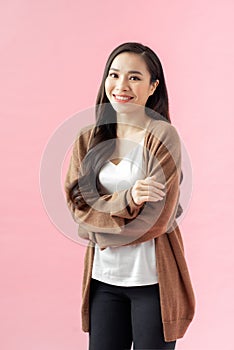 Portrait of a smiling asian businesswoman standing with arms folded and looking at camera isolated over pink background