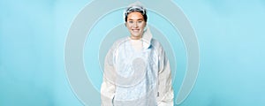 Portrait of smiling asian female doctor or nurse, wearing personal protective equipment and looking happy, standing over