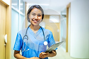 Portrait of smiling asian nurse or female doctor health worker wearing blue uniform holding digital tablet while posing on modern