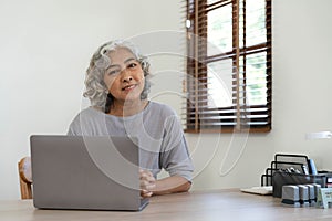 Portrait of smiling asian senior mature middle aged businesswoman using laptop working and web surfing on desk.