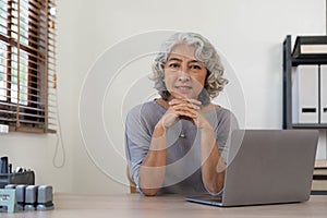 Portrait of smiling asian senior mature middle aged businesswoman using laptop working and web surfing on desk.