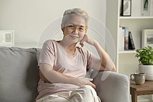 Portrait of smiling Asian senior woman sitting on sofa at home.