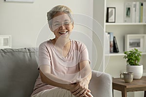 Portrait of smiling Asian senior woman sitting on sofa at home.