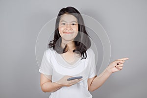 Portrait of smiling Asian teenager wears white t-shirt holding a smartphone and pointing finger to the side