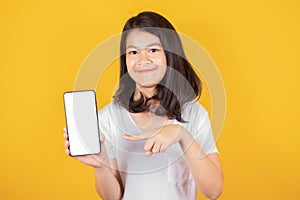 Portrait of smiling Asian teenager wears white t-shirt pointing on blank screen of smart phone isolated on yellow background, Mock