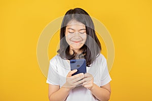 Portrait of smiling Asian teenager wears white t-shirt she is using mobile phone or smartphone isolated on yellow background