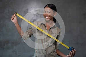 Portrait of smiling Asian woman architect holding measuring tape over concrete wall