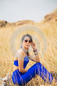 Portrait smiling Asian woman in a blue dress sitting on the ground with dry grass growing on the cost