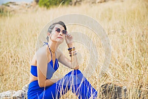 Portrait smiling Asian woman in a blue dress sitting on the ground with dry grass growing on the cost