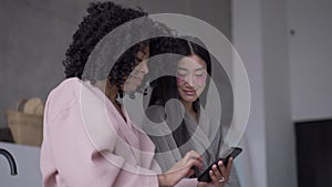 Portrait of smiling Asian woman with eye patches surfing social media on smartphone with African American roommate. Two