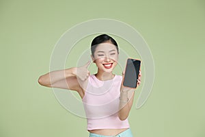 Portrait of smiling asian woman holding smartphone with black blank device screen in hand, showing thumb up gesture