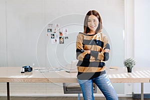 Portrait of smiling Asian woman photographer standing with arms crossed and looking at camera at her studio.Freelance Startup