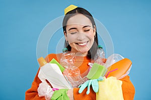 Portrait of smiling asian woman with plastic garbage, holding waste and looks happy, collects litter for recycling